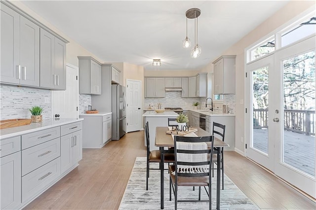 kitchen with french doors, gray cabinets, light wood-style flooring, under cabinet range hood, and stainless steel fridge with ice dispenser