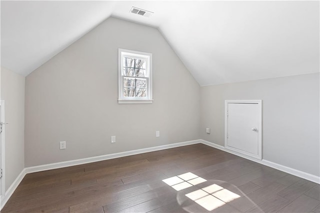 additional living space with dark wood-style flooring, visible vents, vaulted ceiling, and baseboards