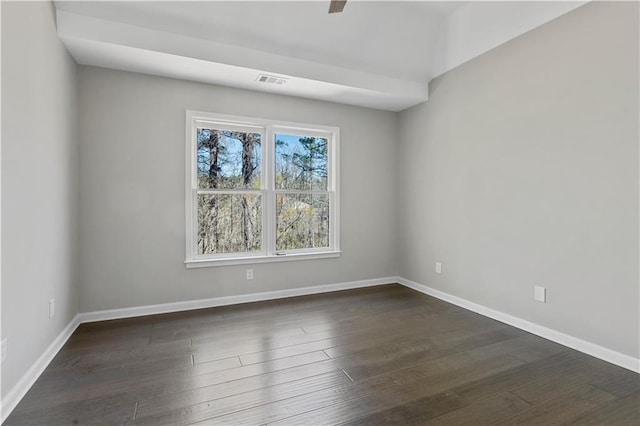 spare room featuring dark wood-style flooring, visible vents, and baseboards