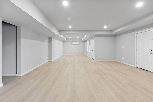 unfurnished room with an AC wall unit, a tray ceiling, light wood-type flooring, and baseboards