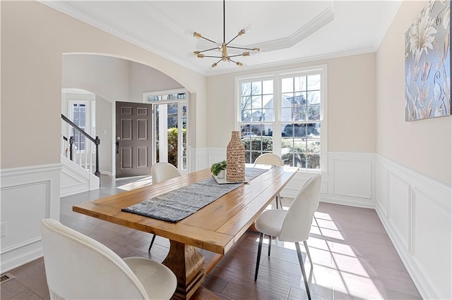 dining area with a wainscoted wall, a raised ceiling, wood finished floors, and a notable chandelier