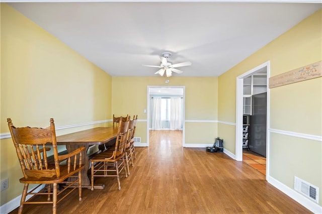 dining space with a ceiling fan, visible vents, baseboards, and wood finished floors