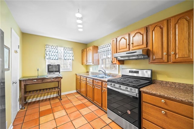 kitchen featuring stainless steel range with gas stovetop, brown cabinets, under cabinet range hood, a sink, and light tile patterned flooring