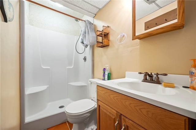 bathroom with toilet, a walk in shower, a paneled ceiling, and vanity