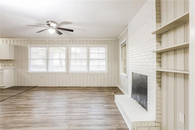 unfurnished living room with ceiling fan, built in features, light hardwood / wood-style flooring, crown molding, and a fireplace