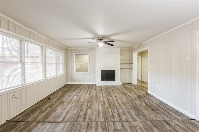 unfurnished living room with ceiling fan, crown molding, a fireplace, hardwood / wood-style floors, and wood walls