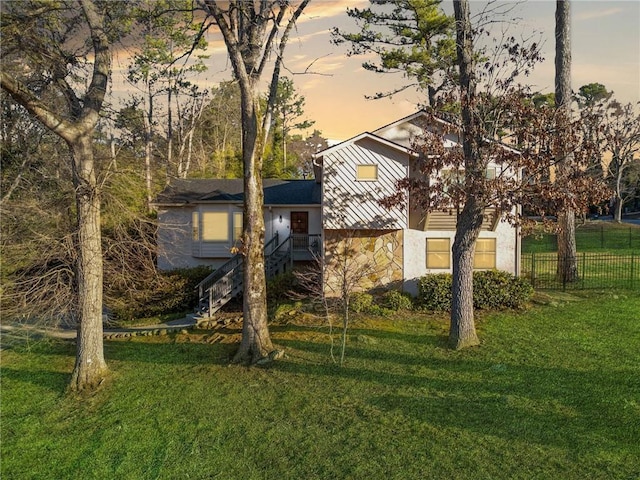 tri-level home with stairs, a front yard, fence, and stone siding