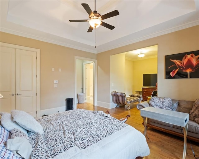 bedroom with hardwood / wood-style floors, ceiling fan, a closet, and a tray ceiling