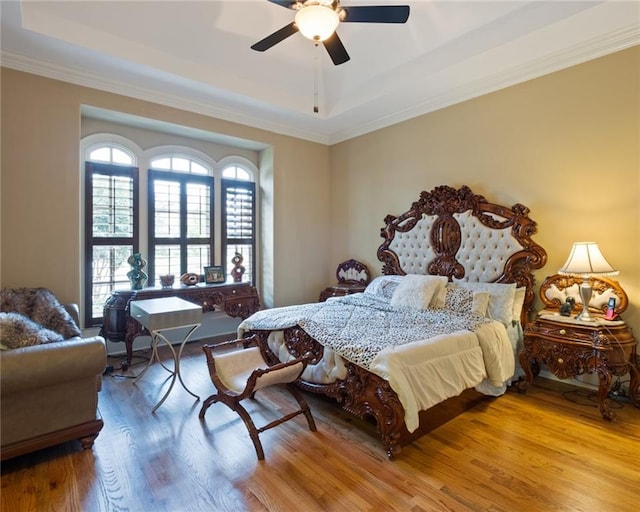 bedroom with light hardwood / wood-style flooring, a raised ceiling, and ceiling fan