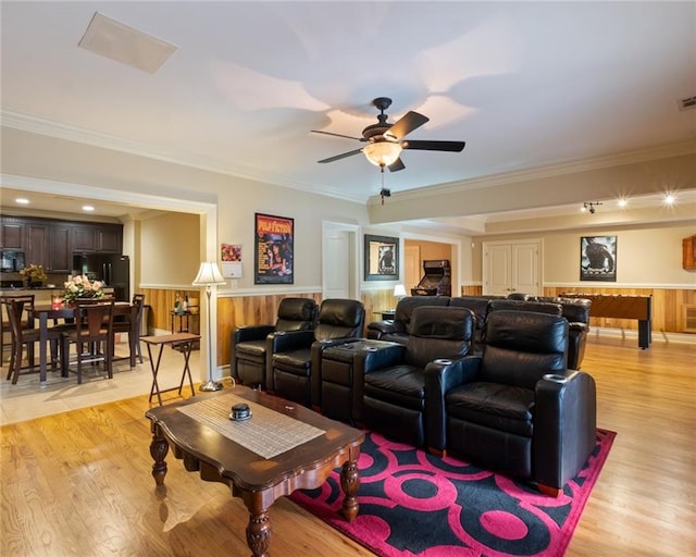 cinema room featuring crown molding, wooden walls, ceiling fan, and light hardwood / wood-style flooring