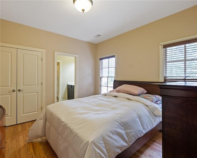 bedroom featuring ensuite bath, a closet, and light hardwood / wood-style flooring