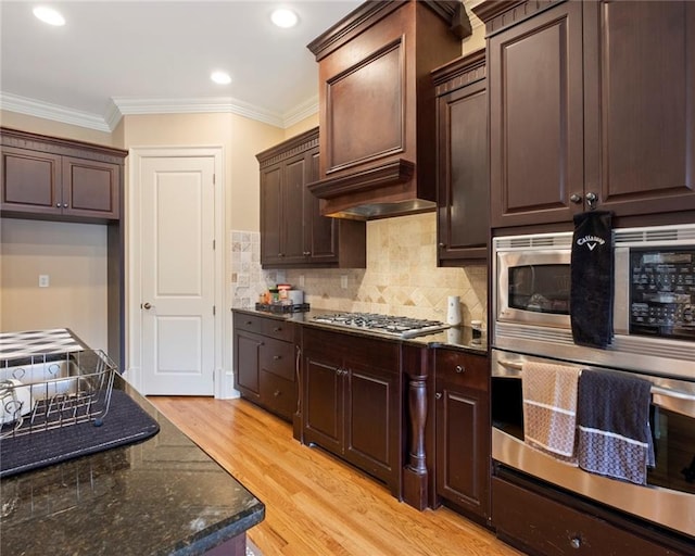 kitchen featuring crown molding, decorative backsplash, dark stone countertops, light wood-type flooring, and stainless steel appliances