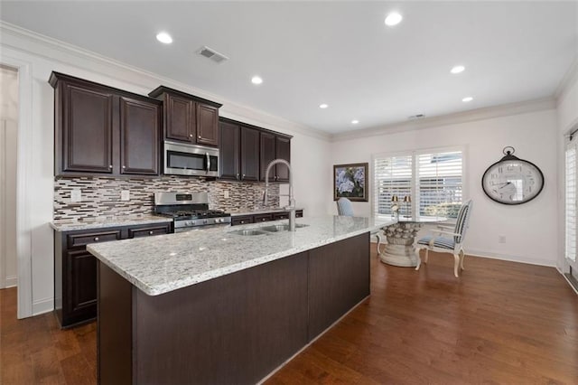 kitchen featuring sink, ornamental molding, an island with sink, appliances with stainless steel finishes, and dark brown cabinetry