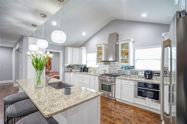kitchen with stainless steel appliances, a breakfast bar, vaulted ceiling, a sink, and wall chimney exhaust hood