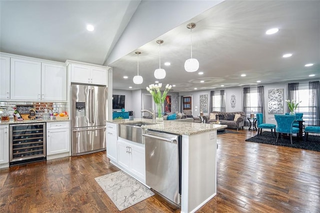 kitchen with lofted ceiling, beverage cooler, light stone countertops, appliances with stainless steel finishes, and open floor plan