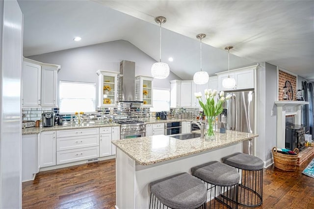 kitchen featuring vaulted ceiling, a sink, white cabinets, wall chimney exhaust hood, and appliances with stainless steel finishes