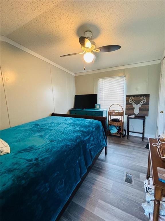 bedroom with a textured ceiling, wood finished floors, visible vents, a ceiling fan, and ornamental molding