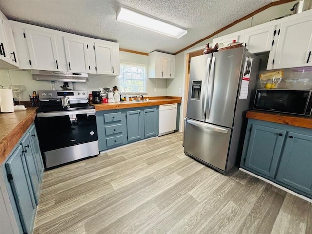 kitchen with lofted ceiling, under cabinet range hood, stainless steel appliances, blue cabinetry, and crown molding