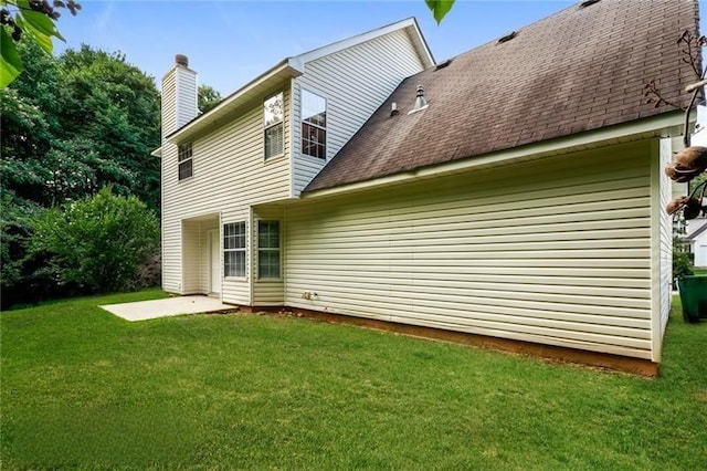 rear view of house with a shingled roof, a chimney, and a yard