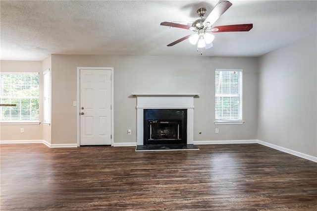 unfurnished living room featuring baseboards, a fireplace with raised hearth, ceiling fan, wood finished floors, and a textured ceiling