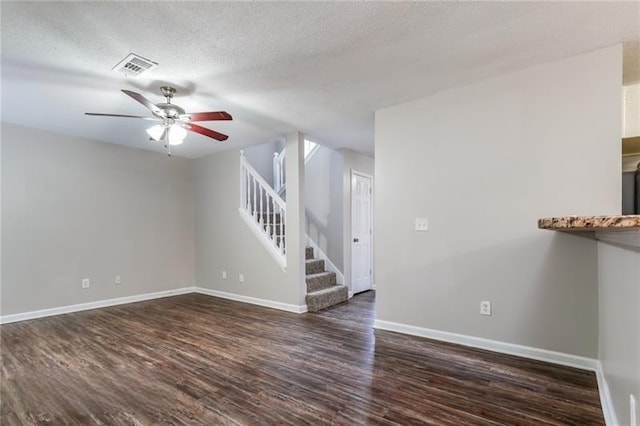 unfurnished room featuring a textured ceiling, visible vents, baseboards, stairway, and dark wood finished floors