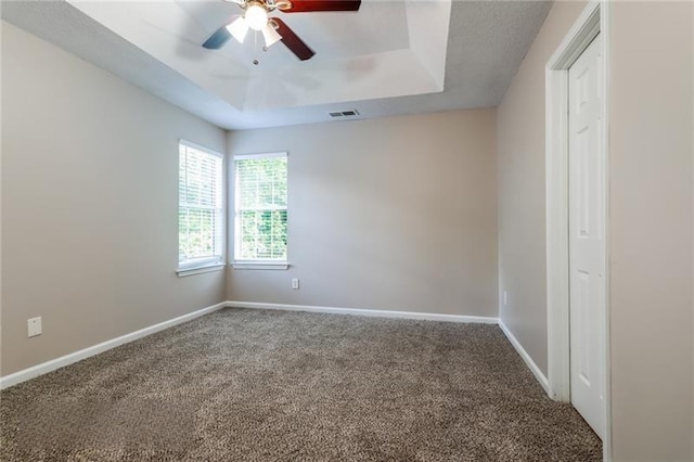 carpeted empty room featuring a tray ceiling, visible vents, ceiling fan, and baseboards