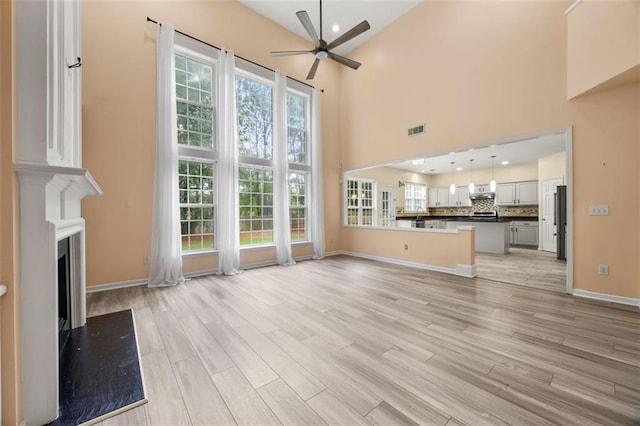 5156 Amberden Hall Dr, Suwanee, GA 30024 - unfurnished living room with a ceiling fan, a towering ceiling, light wood-type flooring, a fireplace, and baseboards