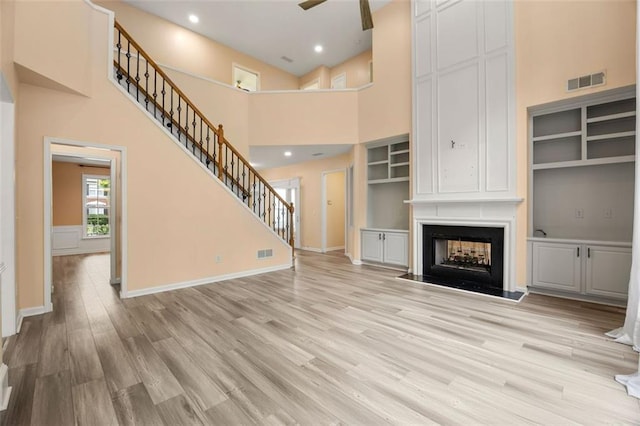 5156 Amberden Hall Dr, Suwanee, GA 30024 - unfurnished living room featuring light wood-style flooring, stairs, a high ceiling, a large fireplace, and built in shelves