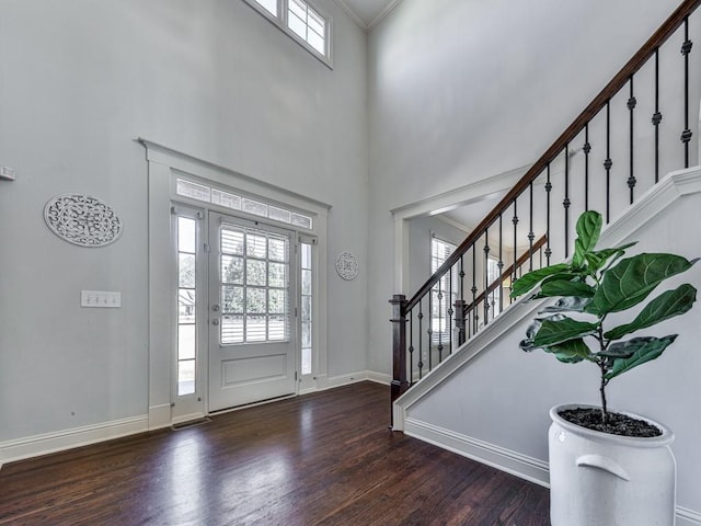 foyer with a towering ceiling, stairway, ornamental molding, wood finished floors, and baseboards