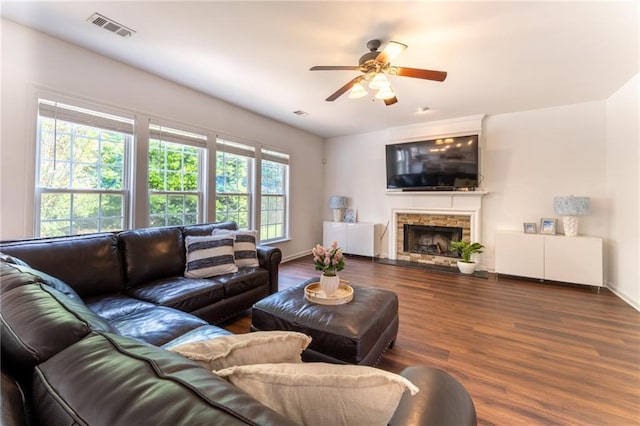 living room featuring a ceiling fan, wood finished floors, a stone fireplace, and baseboards