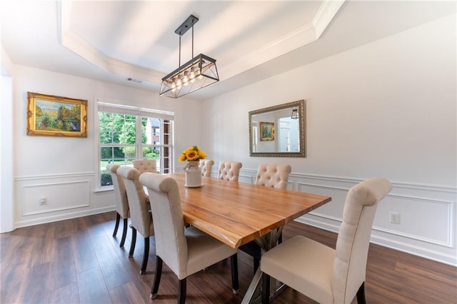 dining room featuring a raised ceiling, ornamental molding, dark wood-style floors, a decorative wall, and wainscoting