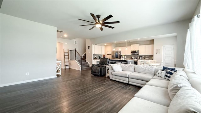 living room featuring ceiling fan, dark wood finished floors, baseboards, visible vents, and stairway