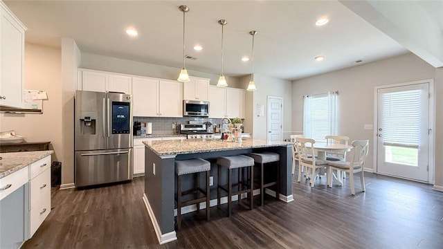 kitchen featuring appliances with stainless steel finishes, a breakfast bar area, white cabinetry, dark wood-type flooring, and backsplash