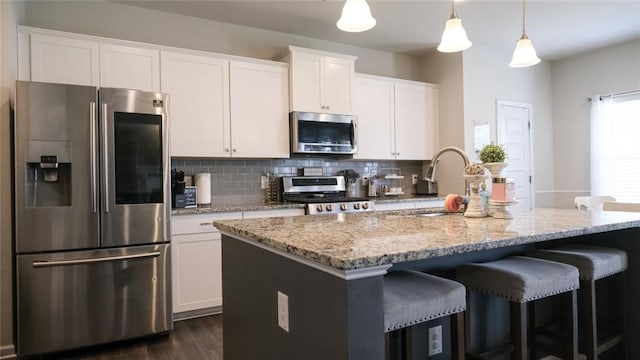 kitchen featuring white cabinets, light stone counters, a kitchen island with sink, stainless steel appliances, and backsplash