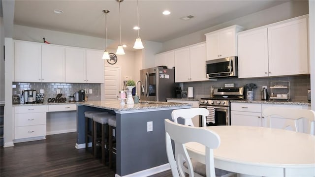 kitchen featuring visible vents, dark wood-style flooring, a center island with sink, tasteful backsplash, and stainless steel appliances