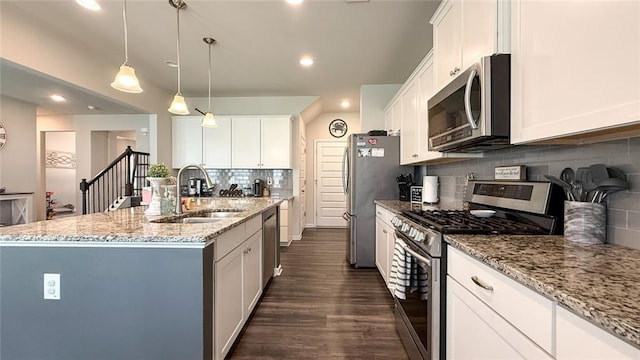 kitchen with decorative backsplash, appliances with stainless steel finishes, light stone countertops, a sink, and an island with sink