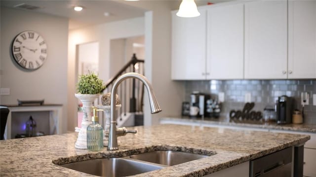 kitchen with white cabinets, light stone counters, a sink, backsplash, and visible vents