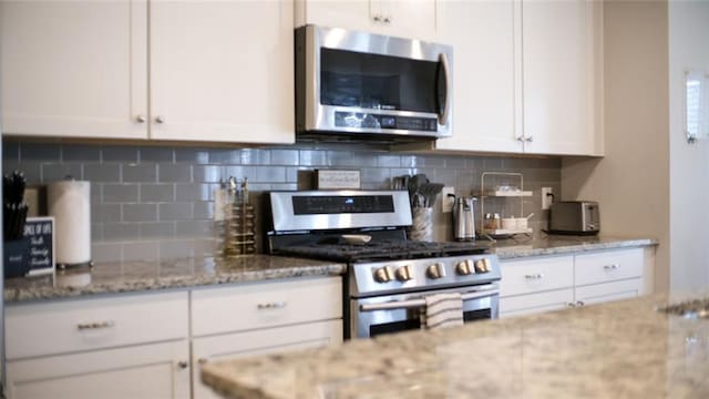 kitchen with light stone counters, tasteful backsplash, stainless steel appliances, and white cabinetry