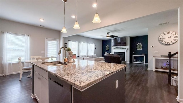 kitchen featuring stainless steel dishwasher, dark wood-style flooring, ceiling fan, light stone counters, and a sink
