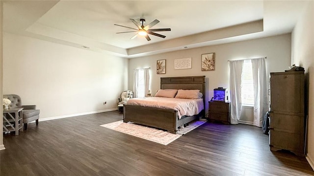 bedroom featuring a raised ceiling, multiple windows, baseboards, and dark wood finished floors