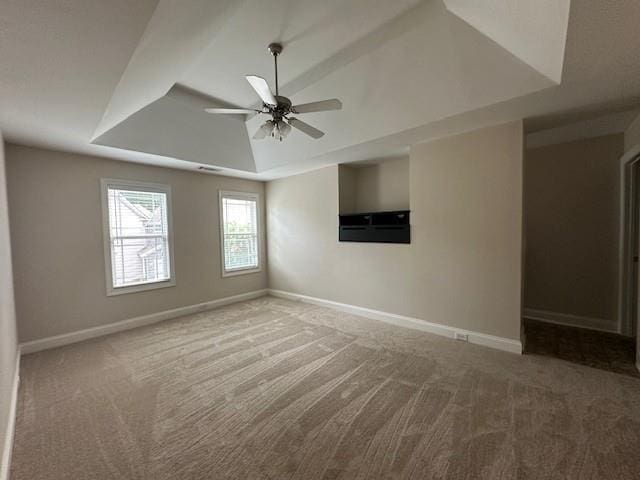 spare room featuring light colored carpet, ceiling fan, and a raised ceiling