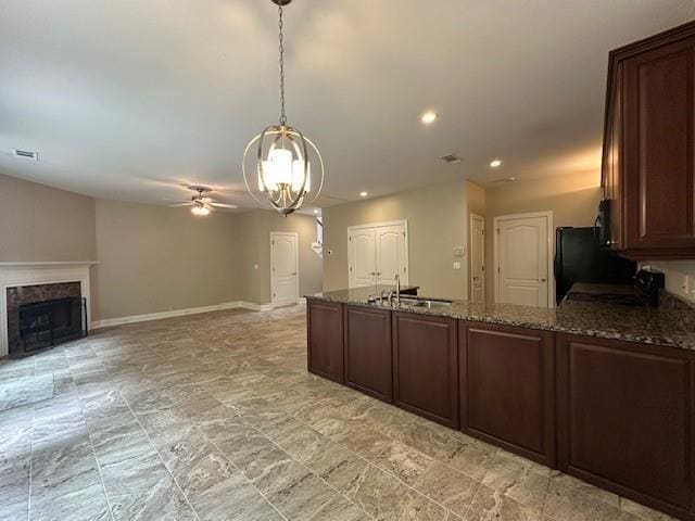 kitchen featuring ceiling fan with notable chandelier, dark stone counters, hanging light fixtures, sink, and a fireplace