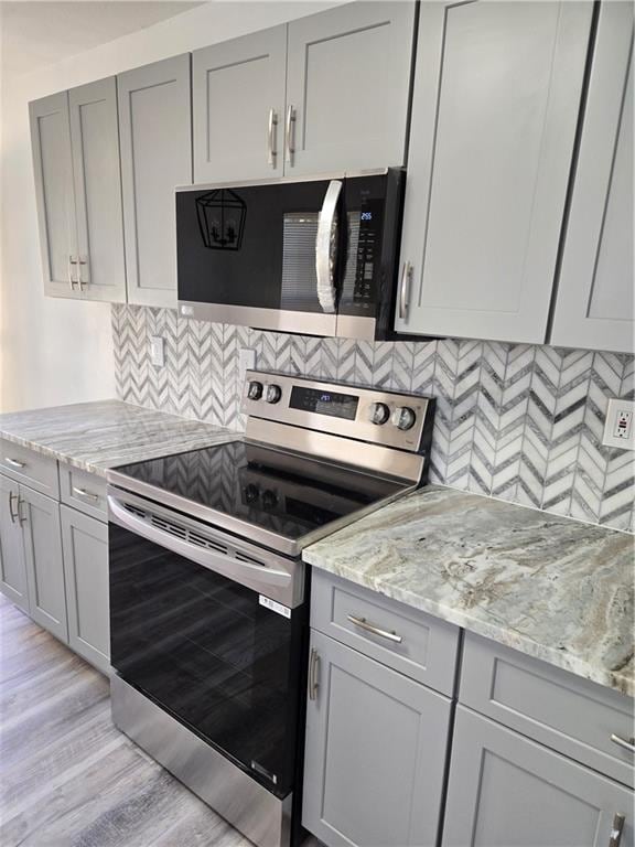 kitchen featuring light stone counters, gray cabinets, decorative backsplash, appliances with stainless steel finishes, and light wood-type flooring