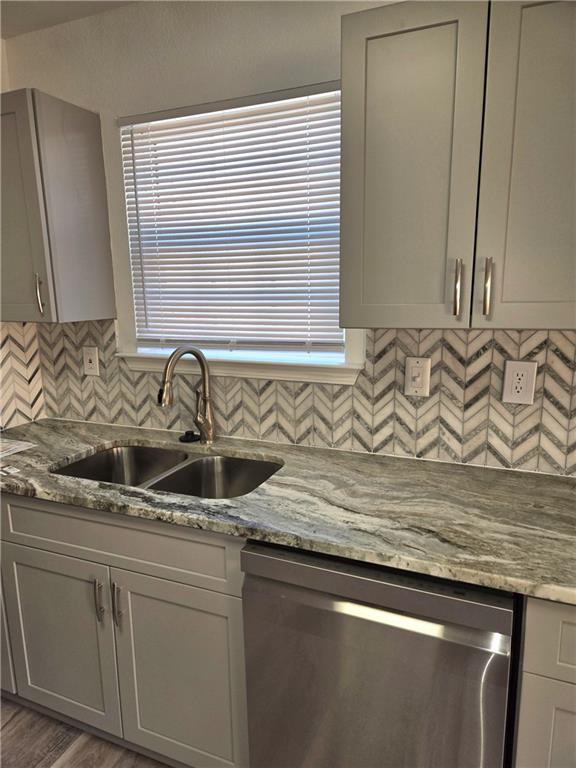 kitchen featuring dishwasher, sink, light stone counters, gray cabinets, and hardwood / wood-style flooring