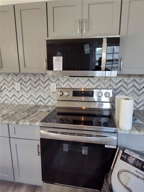 kitchen featuring tasteful backsplash, light stone countertops, light wood-type flooring, and appliances with stainless steel finishes