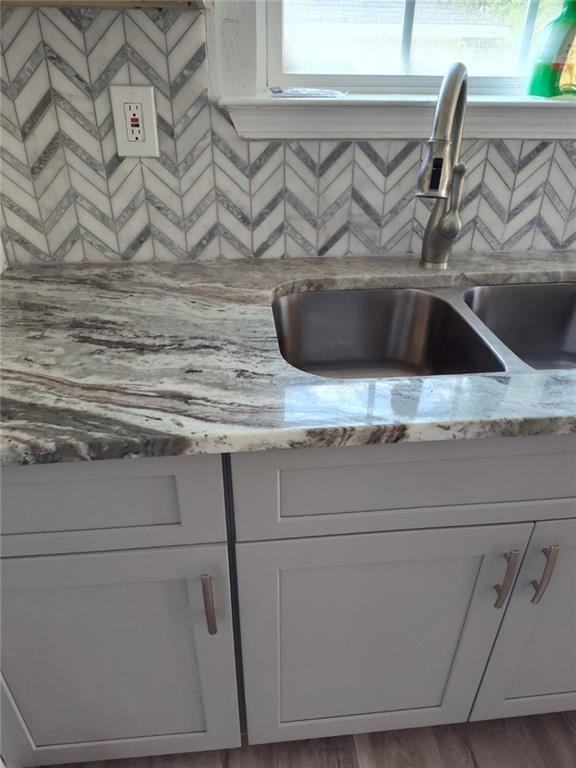 room details with white cabinetry, light stone counters, wood-type flooring, and sink