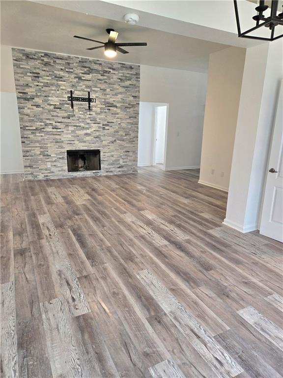 unfurnished living room featuring a fireplace, ceiling fan with notable chandelier, and hardwood / wood-style flooring