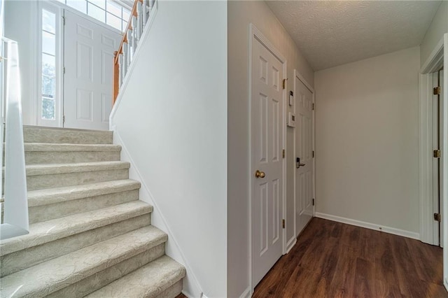 stairs with wood finished floors, baseboards, healthy amount of natural light, and a textured ceiling