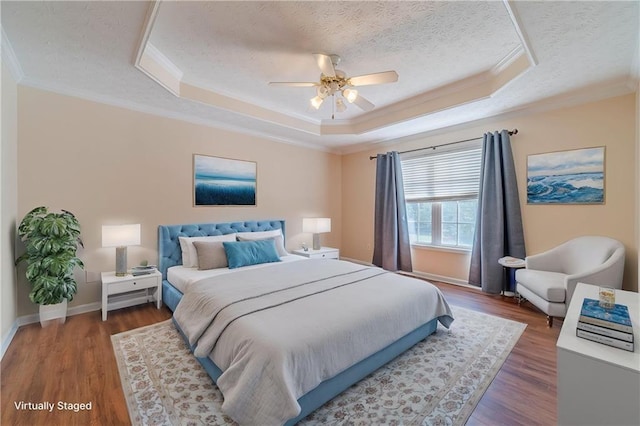 bedroom featuring a raised ceiling, crown molding, wood finished floors, a textured ceiling, and baseboards
