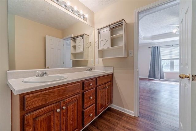 full bath with wood finished floors, double vanity, baseboards, and a textured ceiling